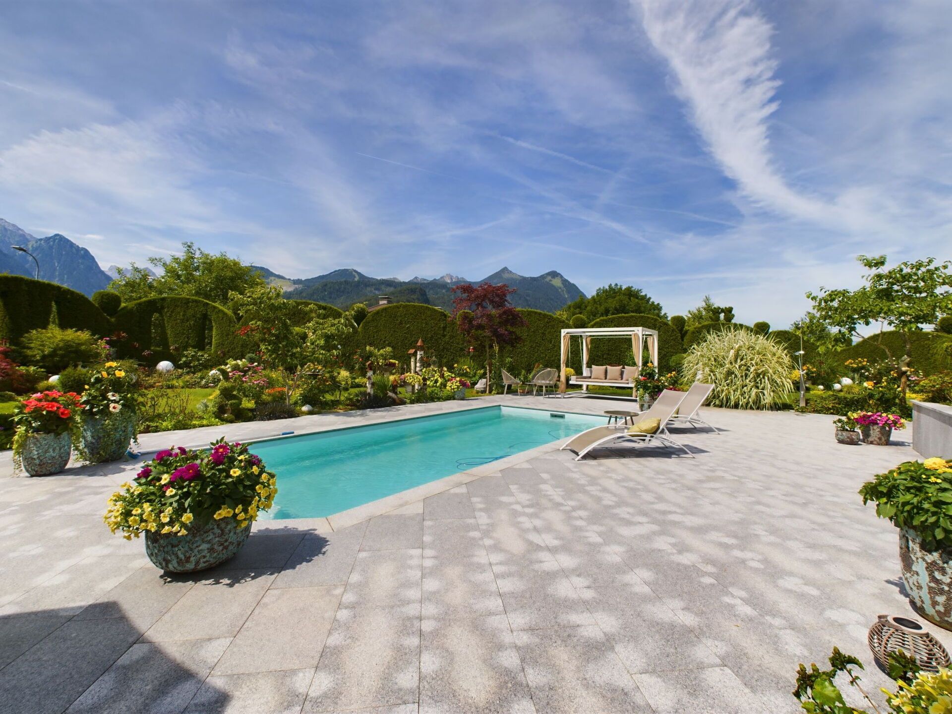 Une piscine entourée de chaises longues, agrémentée de plantes en pot et offrant une vue sur un paysage montagneux.