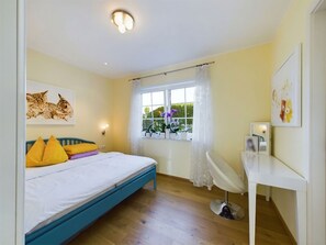 A bedroom with a bed, a bedside table, a chair, a window with curtains, and a ceiling light.