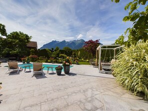 A pool area with chairs, a pergola, and a mountain view.