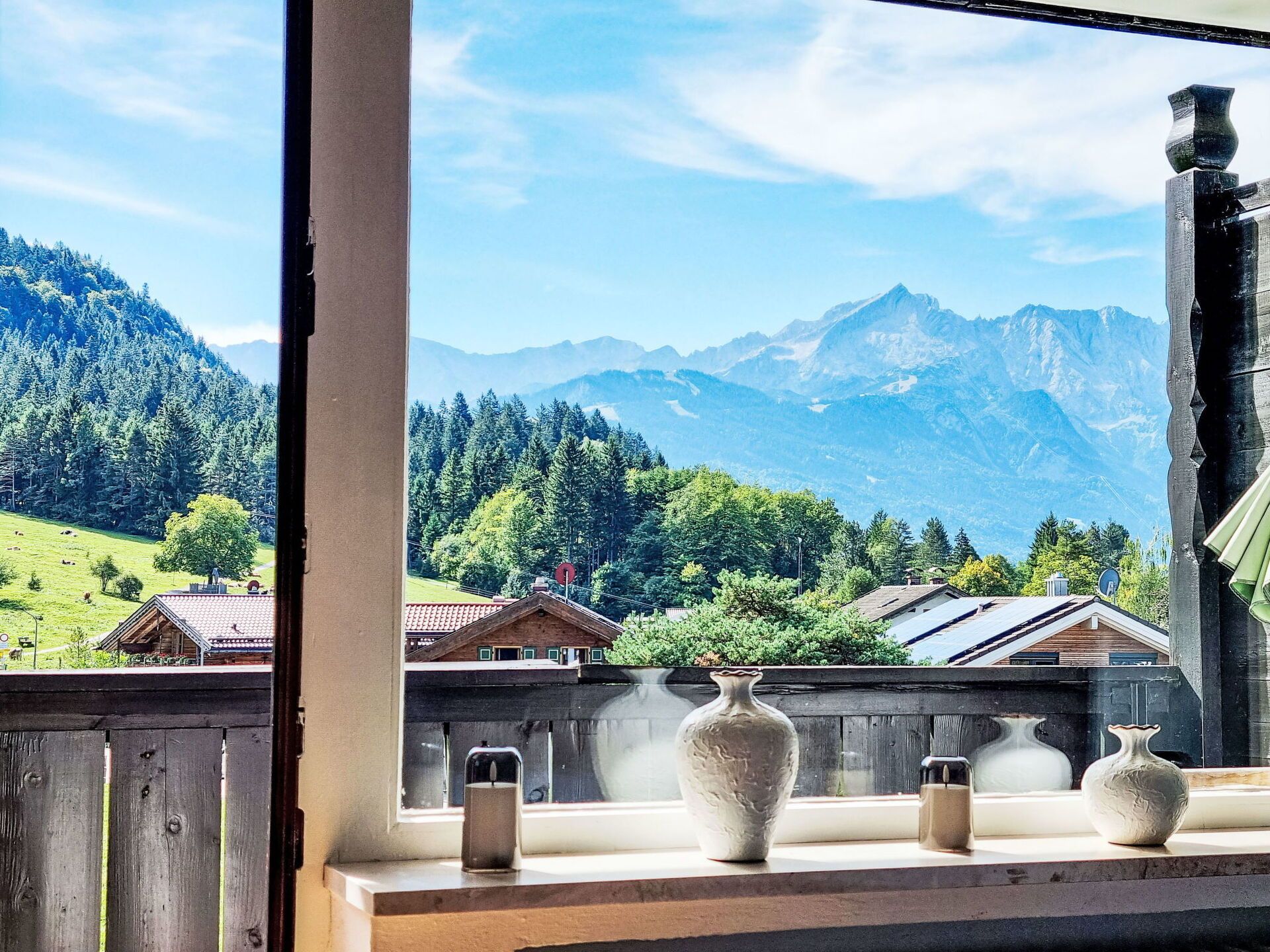A window with a view of a mountainous landscape, a wooden fence, and three vases on the windowsill.