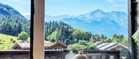 A window with a view of a mountainous landscape, a wooden fence, and three vases on the windowsill.