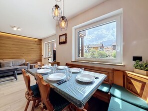 Een eethoek met een tafel voor vier personen, een bankje en uitzicht op een bergachtig landschap door een groot raam.