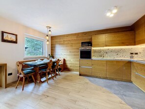 Une cuisine moderne avec des meubles en bois, un four encastré et un coin repas comprenant une table et des chaises.