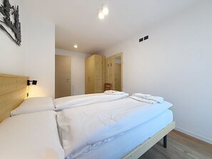 Een tweepersoonsbed met witte lakens, een houten hoofdbord en een nachtkastje met een lamp.