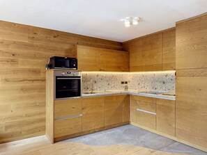Eine moderne Küche mit Holzschränken, einem eingebauten Ofen, einer Mikrowelle und einer Arbeitsplatte aus Granit.