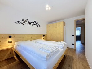Une chambre à coucher avec une tête de lit en bois, un lit recouvert de draps blancs, une armoire en bois et un luminaire fixé au mur.