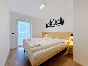 Un dormitorio con cama de madera, ropa de cama blanca, ventana con vistas y decoración de árboles y montañas.