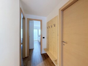 Ein Flur mit Holzboden, einer Tür mit Griff und Blick in ein Schlafzimmer mit Bett und Fenster.