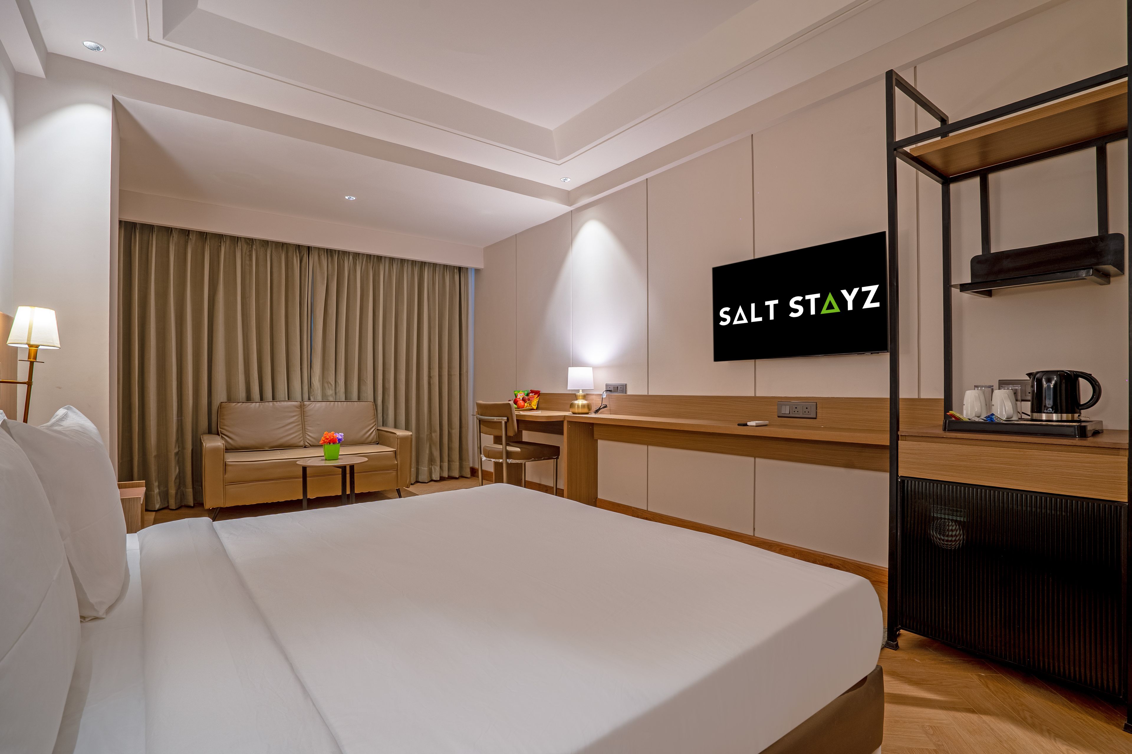 A hotel room with a bed, a desk, a television, and a kitchenette.