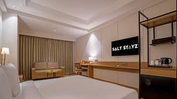 A hotel room with a bed, a desk, a television, and a kitchenette.