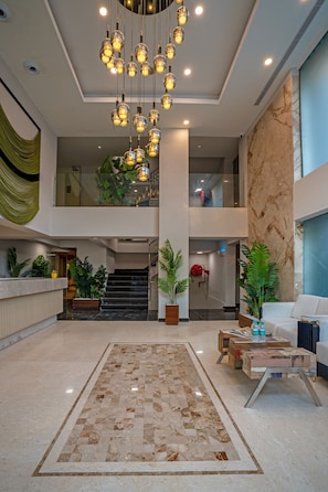 Eine geräumige Lobby mit einer zentralen Treppe, einem Empfangsbereich und einer Sitzecke mit Couchtisch.
