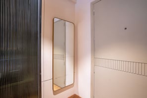 A room with a mirrored wardrobe, a door with a metal bar, and a wall-mounted shelf. - Pause by Saltstayz- East of Kailash (New Delhi)