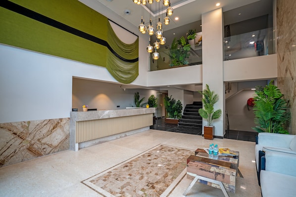 A spacious lobby with a reception desk, a check-in counter, a staircase, and a seating area with a coffee table.