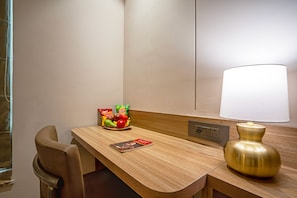 A hotel room with a wooden desk, a lamp, a chair, and a fruit bowl with snacks. - Pause by Saltstayz- East of Kailash (New Delhi)