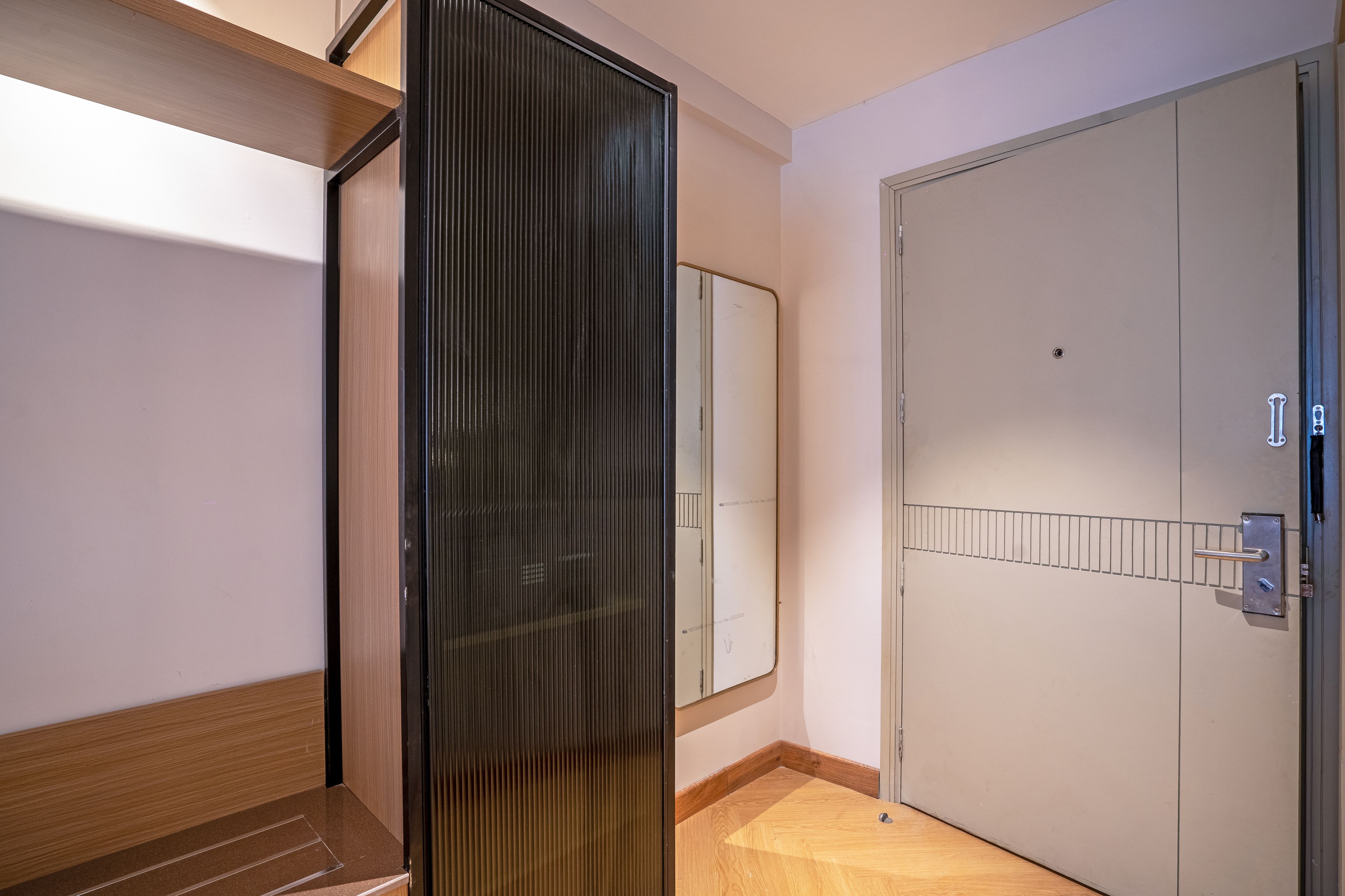 Un pasillo con piso de madera, una puerta de cristal y una puerta blanca con manija de metal.
