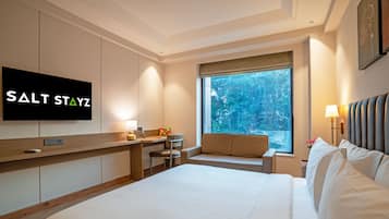 A hotel room with a bed, a desk, a chair, a television, and a window with a view of trees.