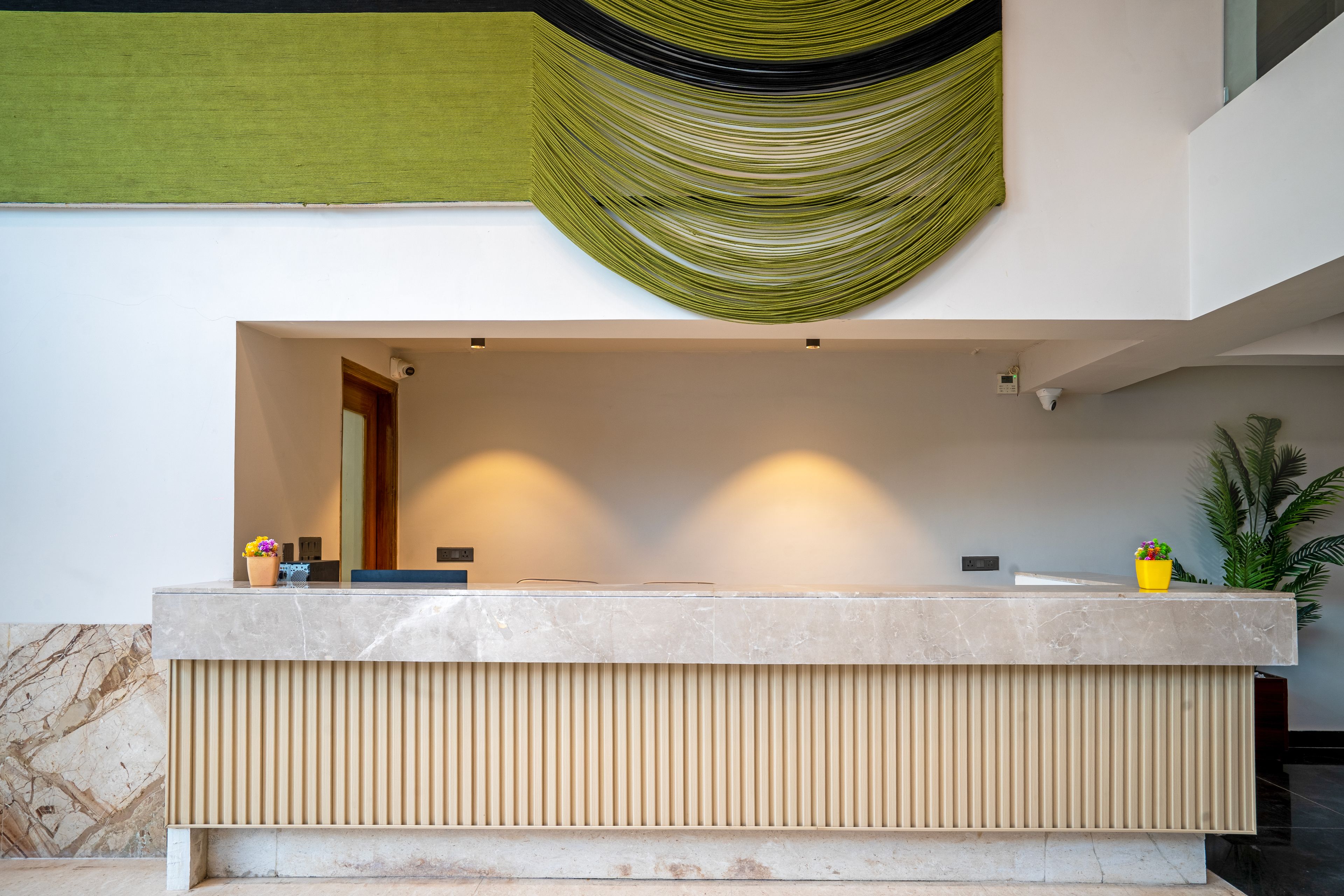 A reception desk with a marble countertop, a vertical wooden slat design, and a green fabric hanging above.