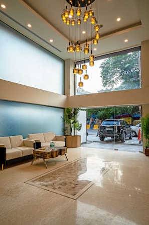 Un hall d’entrée spacieux avec un plafond haut, une grande fenêtre, un canapé, une table basse et un luminaire suspendu.