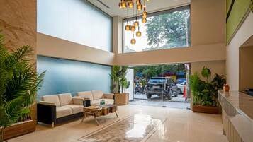 A spacious lobby with a high ceiling, a seating area with a sofa and coffee table, and a view of the street through a large window.