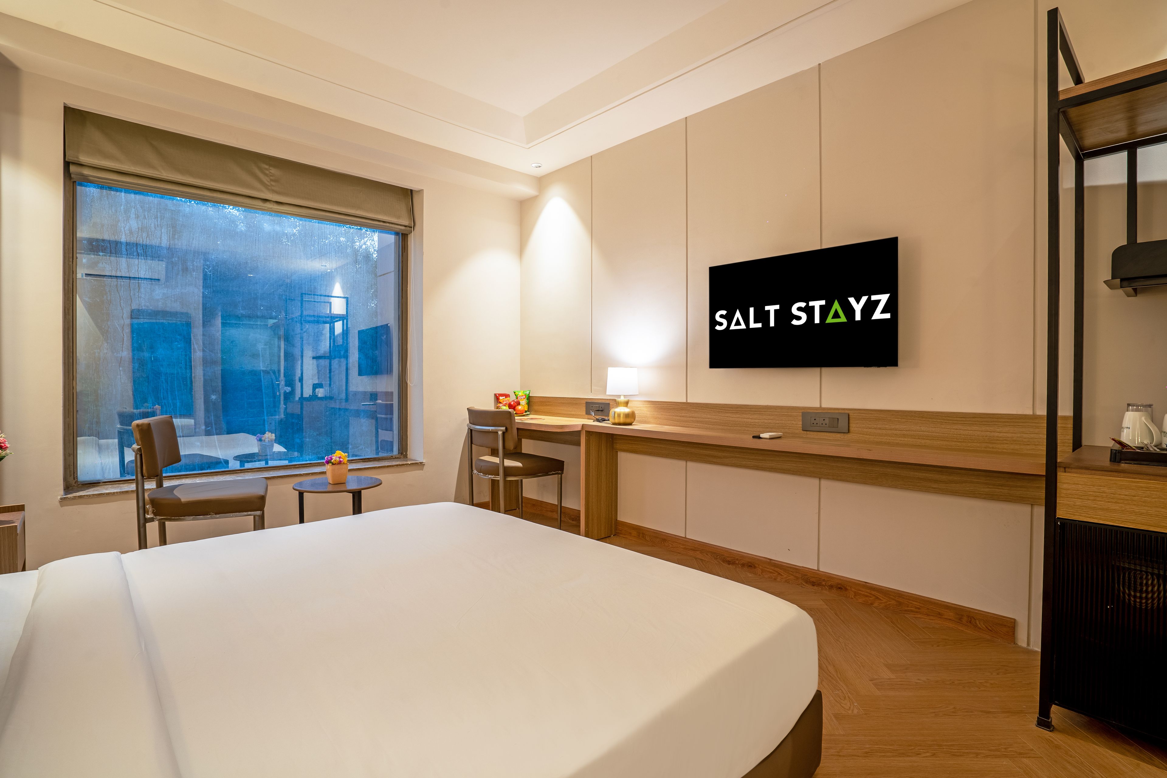 Habitación de hotel con cama, escritorio, silla, televisor montado en la pared y ventana con vistas a la ciudad.