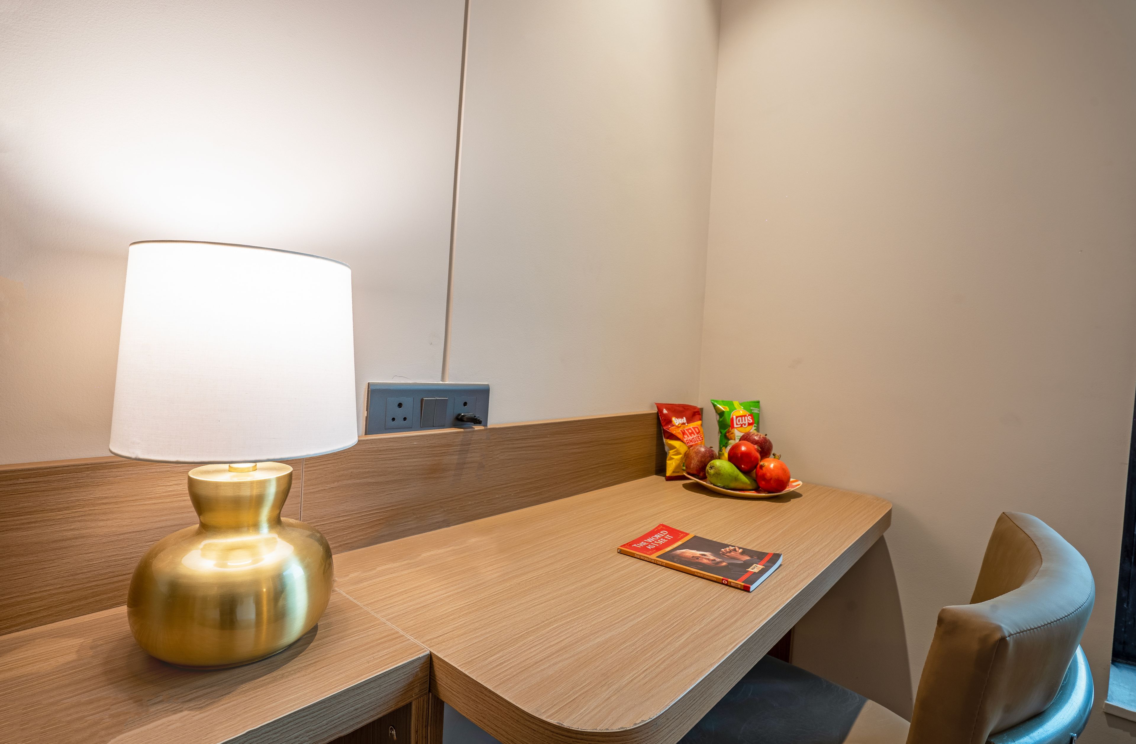A hotel room with a wooden desk, a lamp, a plate of fruit, and a book.