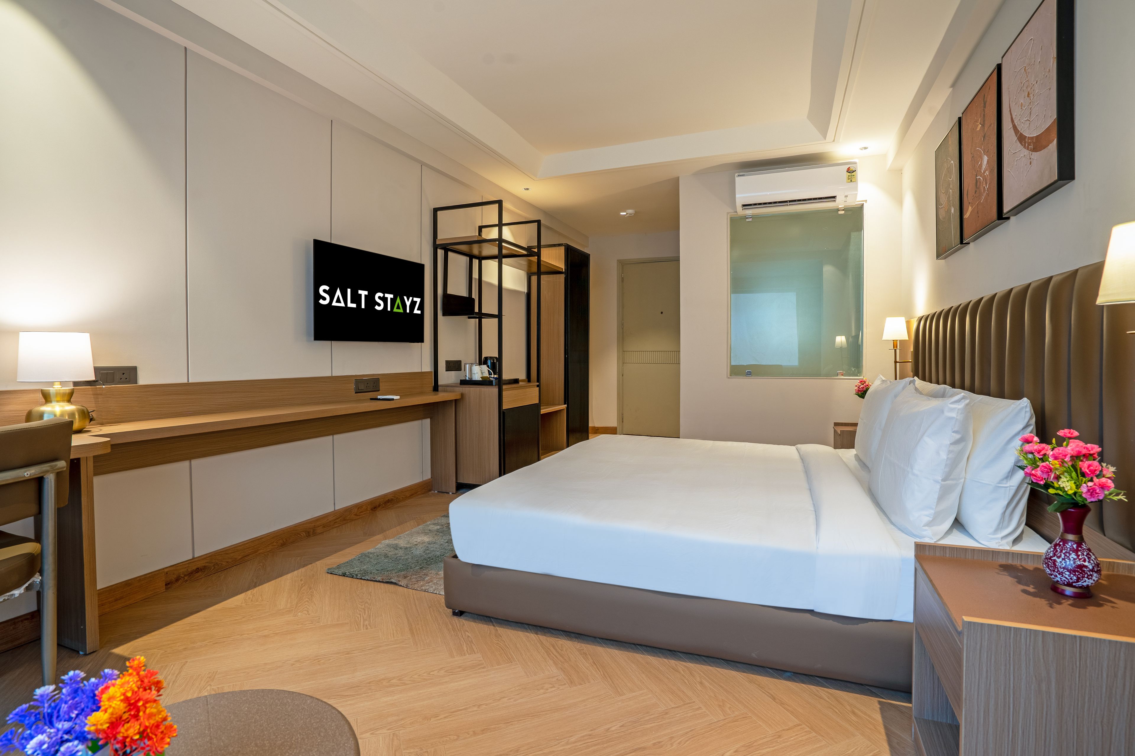 Habitación de hotel con cama, escritorio, silla, televisor y aire acondicionado instalado en la pared.