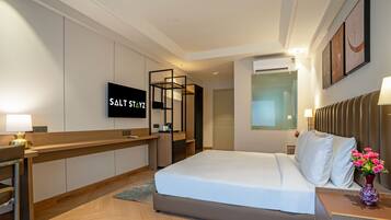 Habitación de hotel con cama, escritorio, silla, televisor y aire acondicionado instalado en la pared.