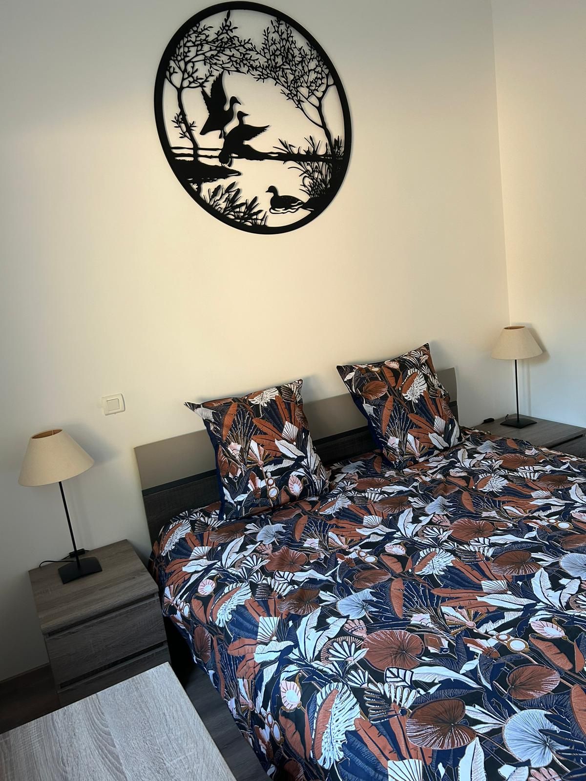 Une chambre à coucher avec un lit, deux tables de chevet, une lampe et un élément décoratif mural.
