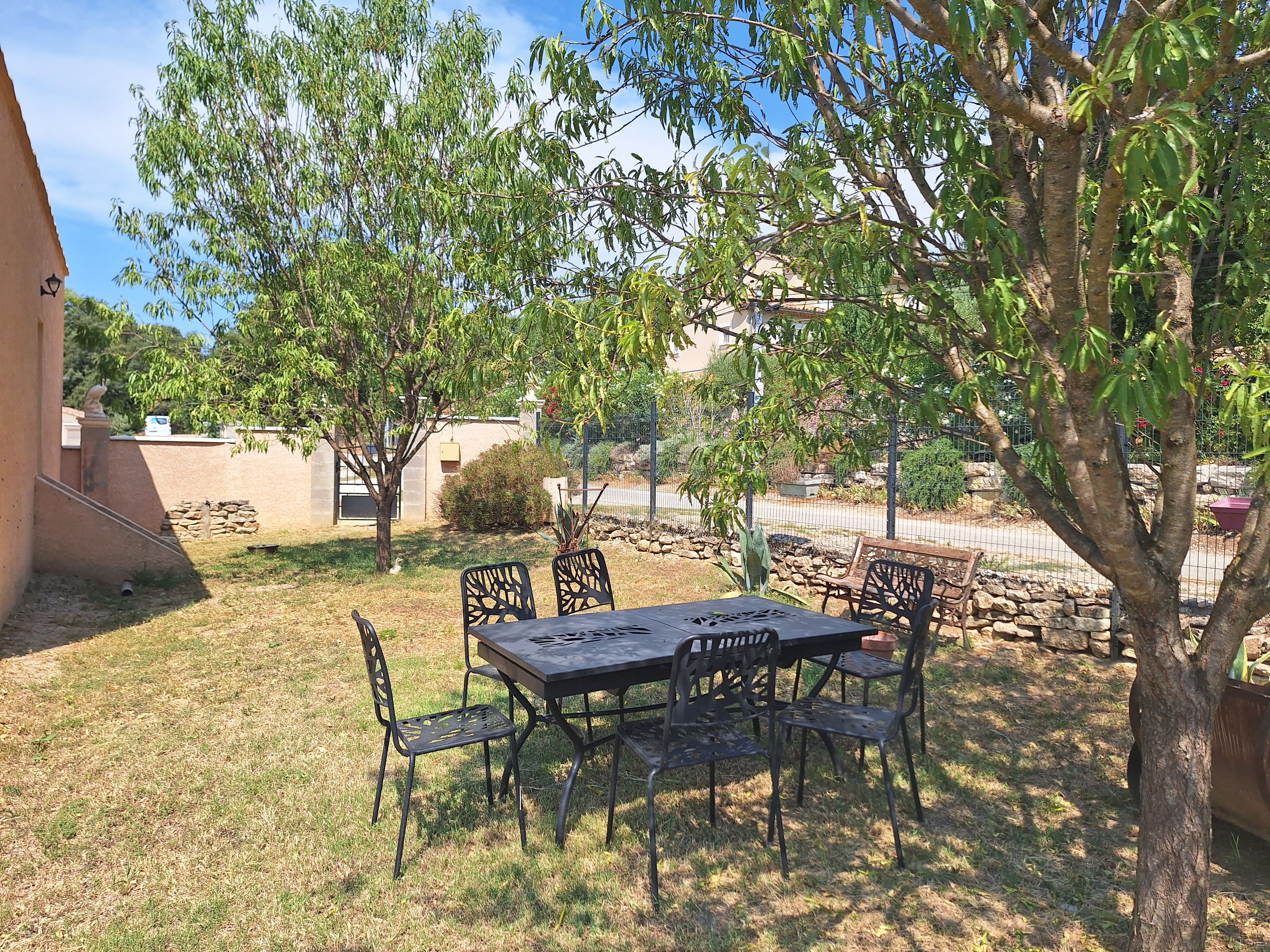 Une terrasse extérieure avec une table et des chaises, entourée d’arbres et d’un mur en pierre.