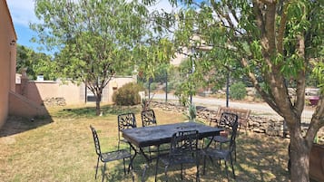 Une terrasse extérieure avec une table et des chaises, entourée d’arbres et d’un mur en pierre.