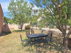 Une terrasse extérieure avec une table et des chaises, entourée d’arbres et d’un mur en pierre.