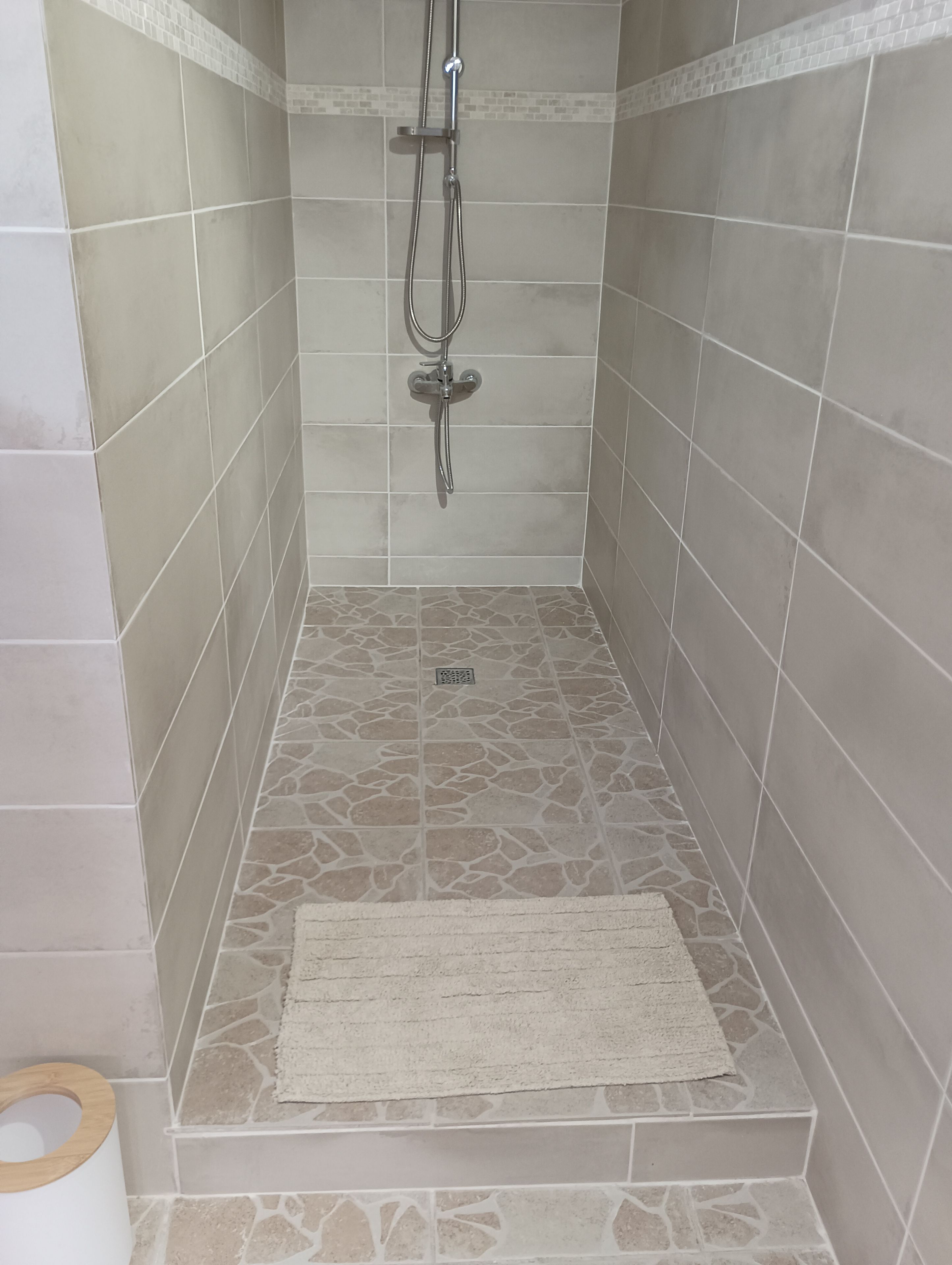 Un espace douche avec des murs et un sol carrelés, une pomme de douche et un drain.