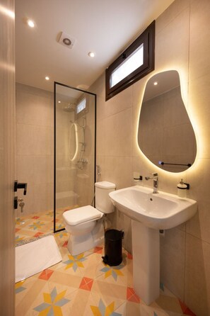 Ein modernes Badezimmer mit einer Duschkabine, einer weißen Toilette, einem Waschbecken mit Spiegel und einem Musterboden.
