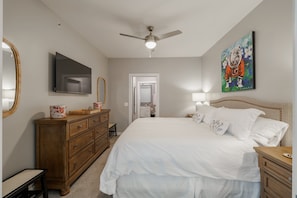 Ein Schlafzimmer mit Bett, Schminktisch, Fernseher, Deckenventilator und Kunstwerken.