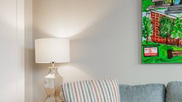 A modern living room with a grey sofa, a striped pillow, a lamp on a wooden side table, and a framed painting on the wall.