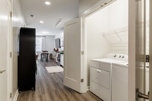 A laundry room with a washing machine, a drying rack, and a door leading to a kitchen area with a dining table and chairs. - The Athens Social - walk to downtown! (Athens)