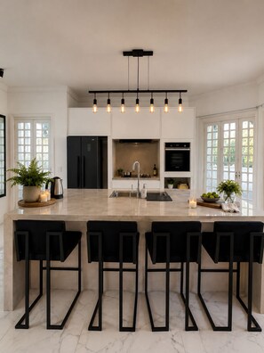 A modern kitchen with a central island, black bar stools, and pendant lighting. - A different Rio experience | Exclusive house with 4 suites near Barra. (Rio de Janeiro)