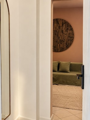 Un couloir avec un miroir, une décoration murale ronde en bois, un canapé vert et un tapis à motifs.