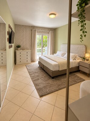 Une chambre à coucher avec un lit, des tables de chevet, une commode, un miroir et un téléviseur fixé au mur.