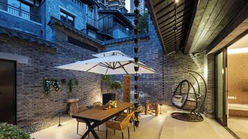 Un patio exterior con mesa y sillas de madera, una silla colgante y un paraguas grande.