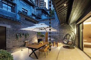Une terrasse extérieure avec une table et des chaises en bois, un fauteuil suspendu et un grand parasol.