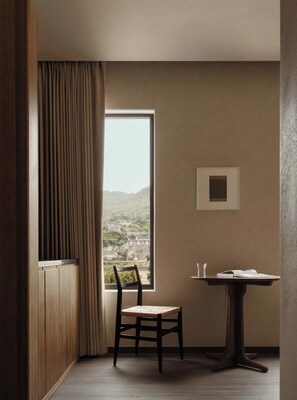 A room with a view of a cityscape through a large window, a wooden chair, a small table with a book and a glass, and a framed picture on the wall. - Daily Fortune  Tianshun River View Villa (Chongqing)
