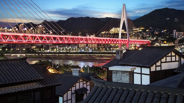 A modern cable-stayed bridge with red lighting, a river below, and traditional buildings in the foreground. - Daily Fortune  Tianshun River View Villa (Chongqing)
