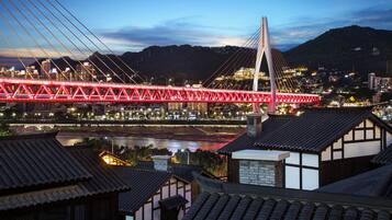 Un moderno puente atirantado con iluminación roja, un río debajo y edificios tradicionales al frente.