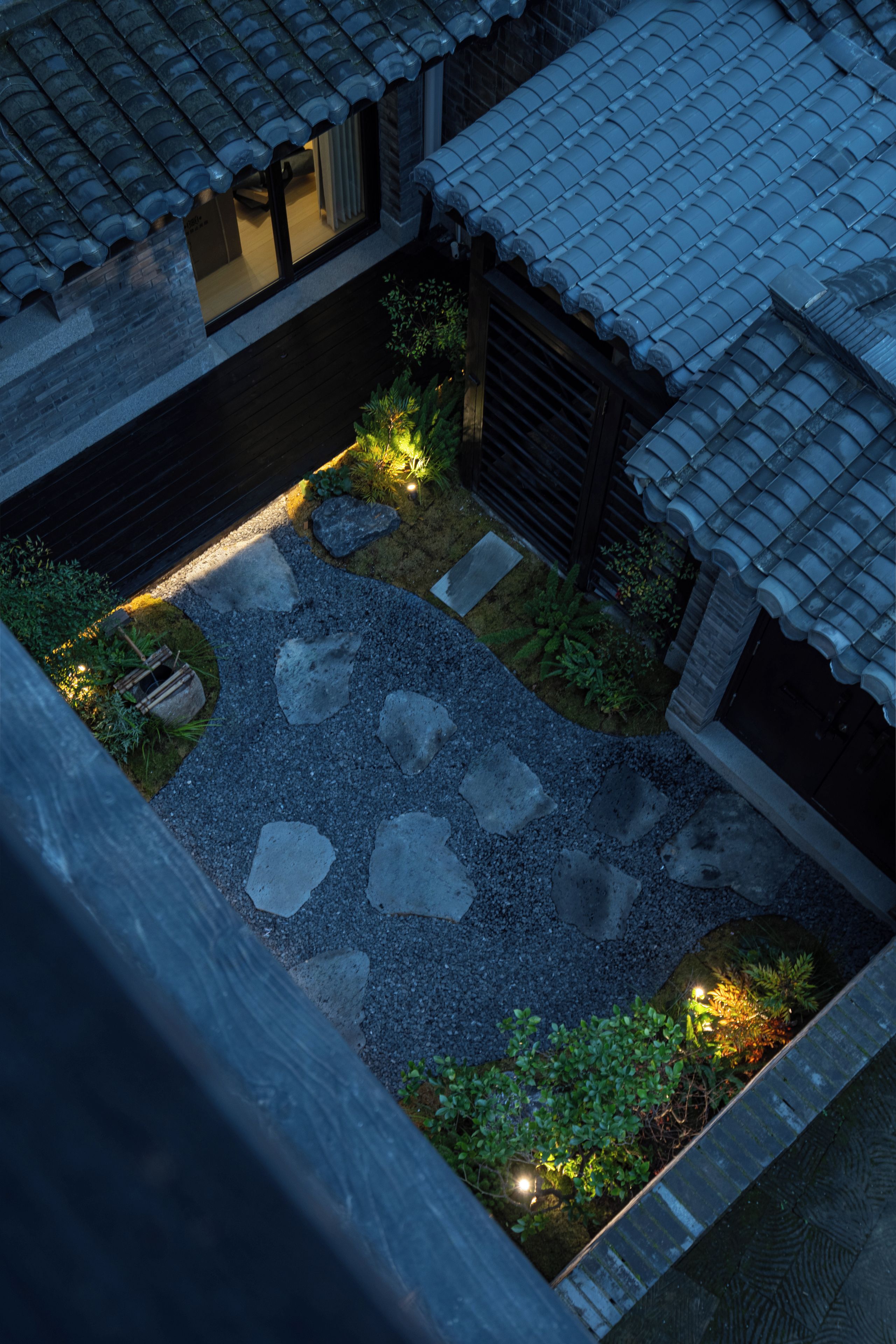 Un patio con pavimento de piedra, cerca de madera y plantas pequeñas.