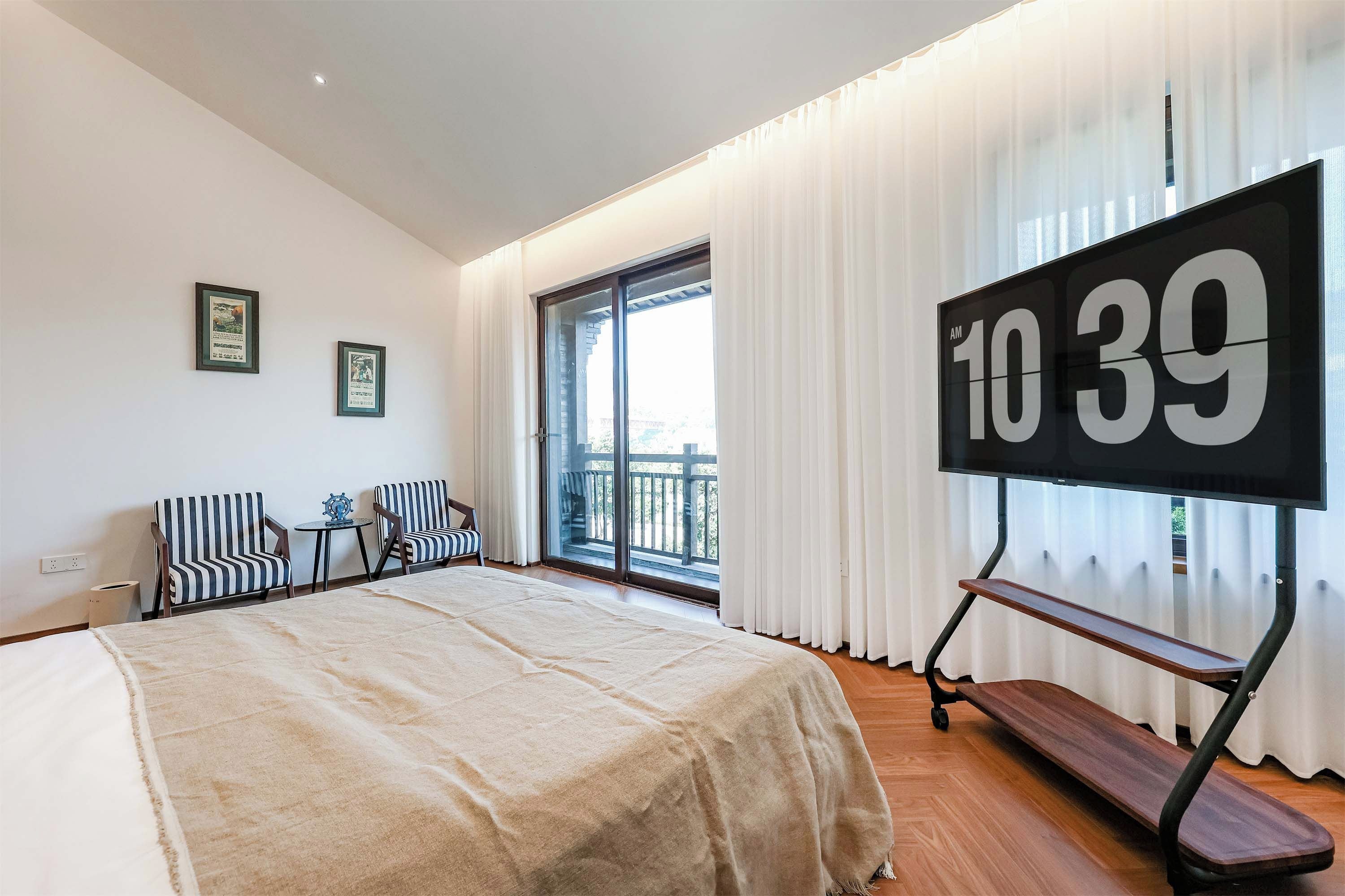 Habitación de hotel con cama, dos sillones, una mesa, televisión y vistas al balcón.