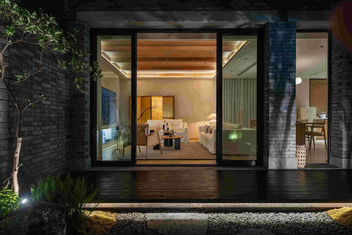 Une maison moderne dotée d’une porte vitrée qui donne sur un espace de vie comprenant un canapé, une table basse et une table à manger.