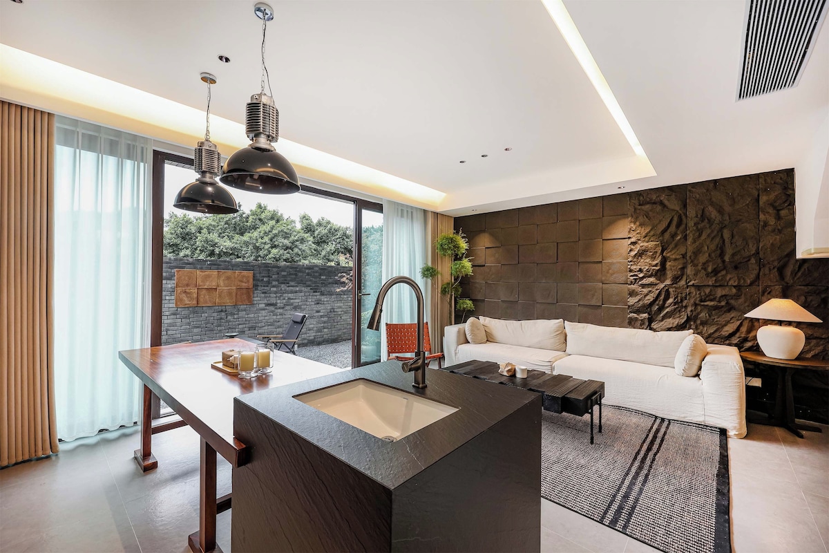 Une cuisine moderne avec un îlot central, un coin repas comprenant une table et des chaises, un canapé et une grande fenêtre agrémentée de rideaux.