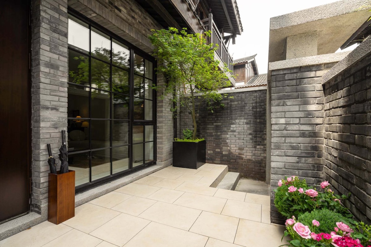 Un bâtiment moderne doté de grandes fenêtres en verre, d’une façade en briques et d’un petit jardin agrémenté de fleurs roses.