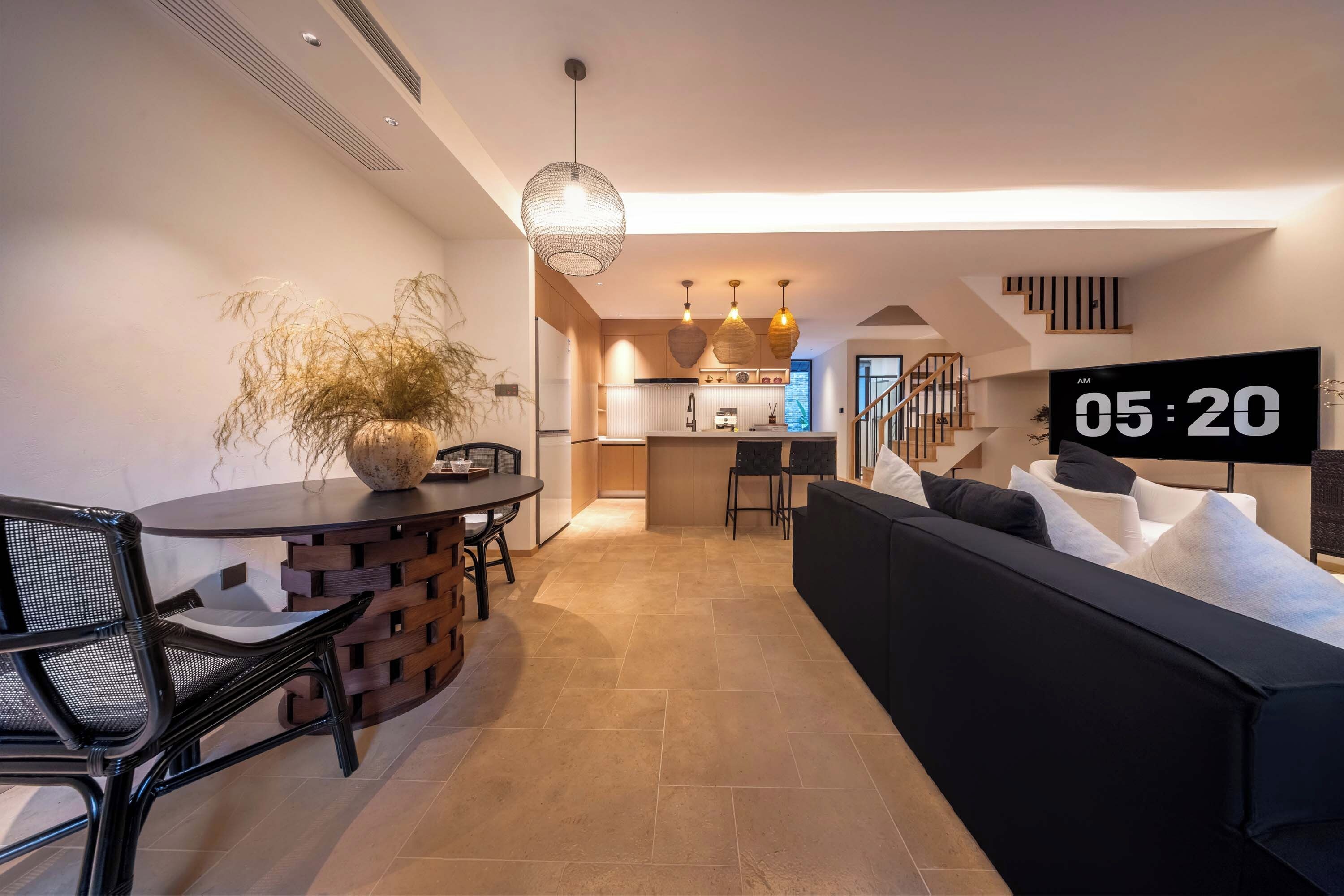 Una sala de estar moderna con un sofá negro, una mesa de comedor con sillas y una cocina al fondo.